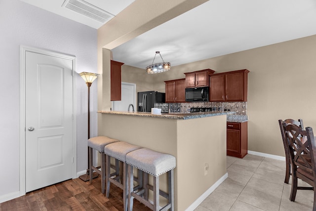 kitchen featuring visible vents, a breakfast bar, black microwave, fridge with ice dispenser, and backsplash