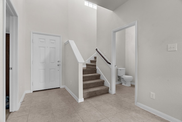 foyer entrance with light tile patterned floors, stairs, and baseboards