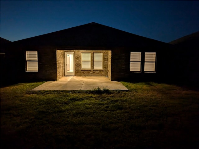 back of house at night featuring a patio area and a lawn