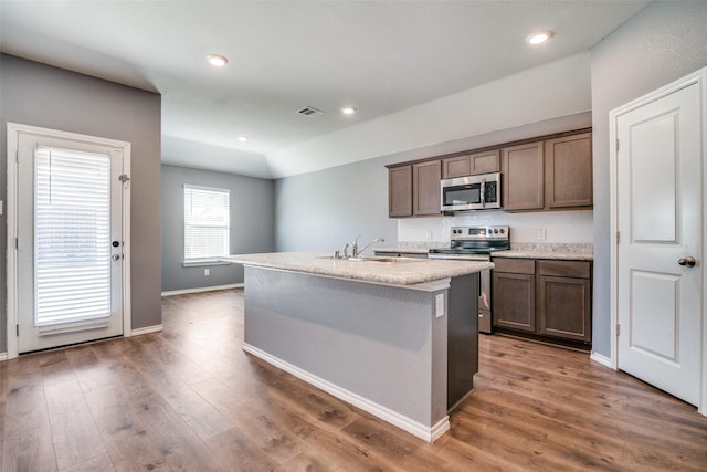 kitchen with baseboards, appliances with stainless steel finishes, wood finished floors, and an island with sink