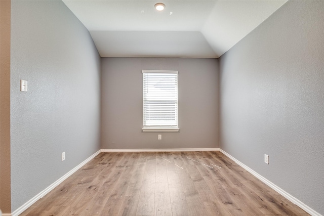 spare room with a textured wall, baseboards, light wood-style flooring, and vaulted ceiling