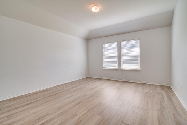 empty room featuring baseboards, lofted ceiling, and light wood-style floors