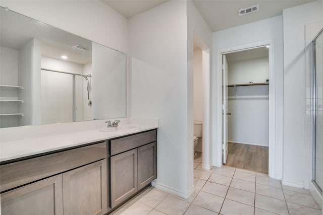 full bathroom with visible vents, a shower stall, a walk in closet, toilet, and vanity