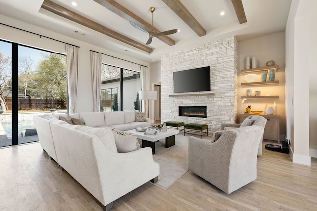 living room featuring ceiling fan, a fireplace, beam ceiling, and light wood-type flooring
