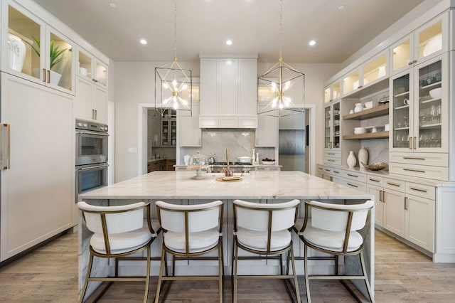 kitchen featuring double oven, tasteful backsplash, a kitchen island with sink, white cabinets, and recessed lighting