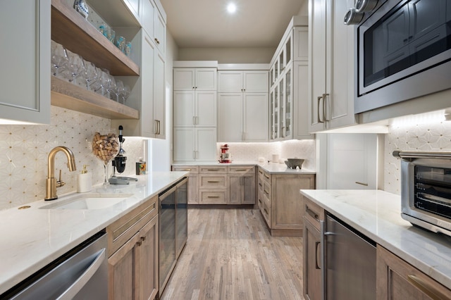 kitchen featuring stainless steel appliances, a sink, wine cooler, light stone countertops, and light wood-type flooring