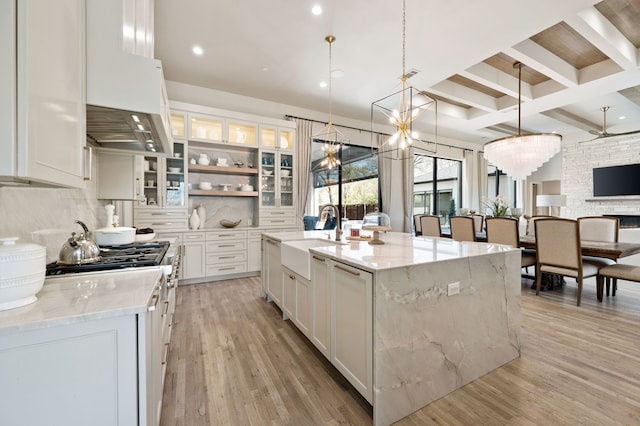 kitchen with a sink, premium range hood, backsplash, white cabinets, and light wood-style floors