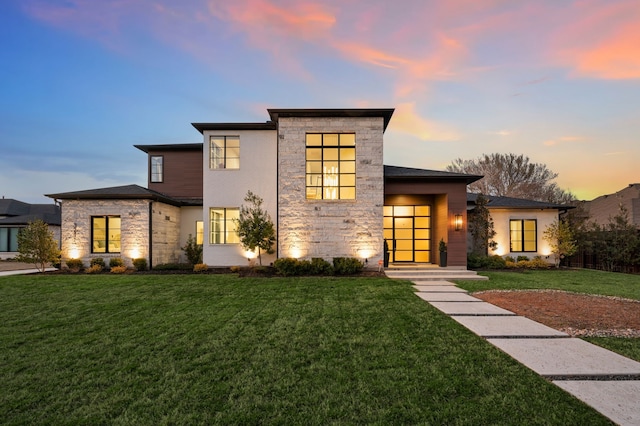 contemporary house with stone siding and a yard