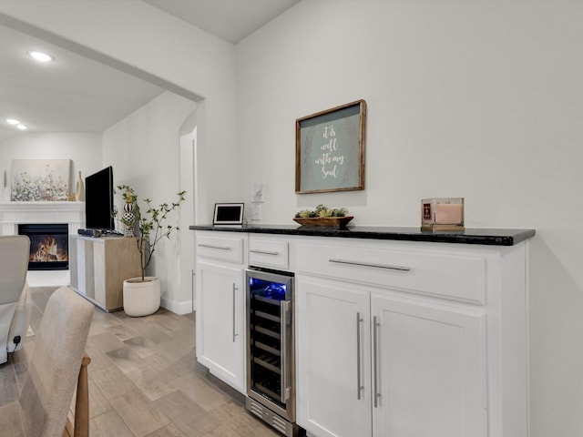bar featuring light wood-style flooring, recessed lighting, beverage cooler, a glass covered fireplace, and bar