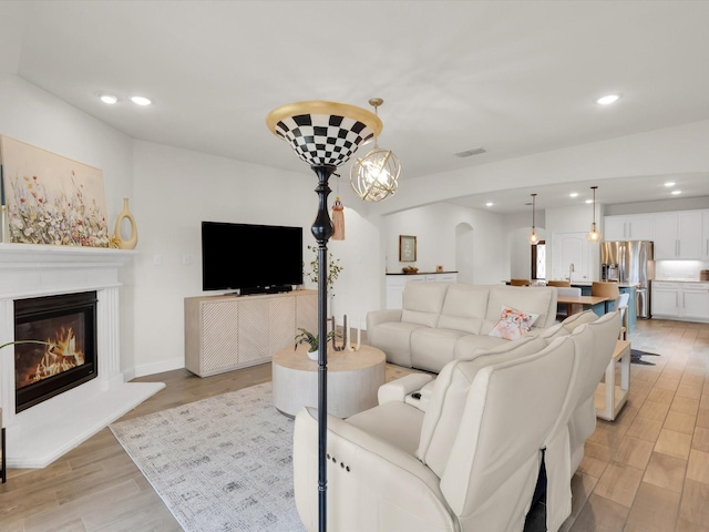 living room with recessed lighting, light wood finished floors, a glass covered fireplace, visible vents, and arched walkways