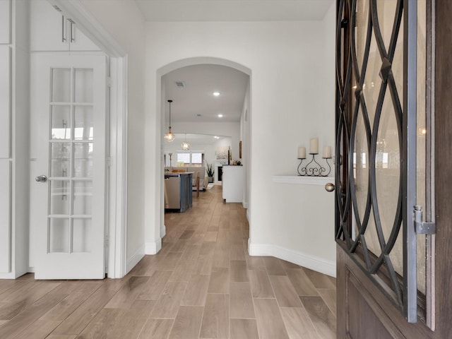 foyer featuring light wood finished floors, baseboards, and arched walkways