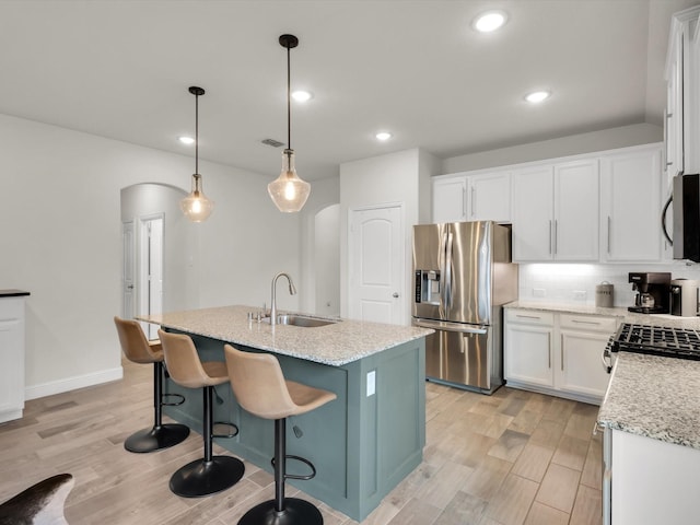 kitchen featuring light wood finished floors, a sink, decorative backsplash, arched walkways, and appliances with stainless steel finishes