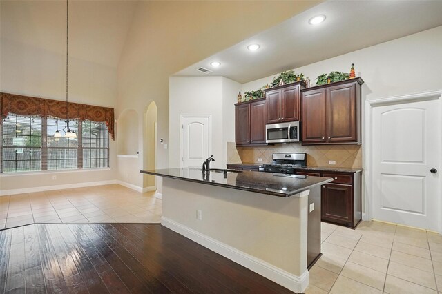 kitchen with a kitchen island with sink, backsplash, appliances with stainless steel finishes, arched walkways, and a sink