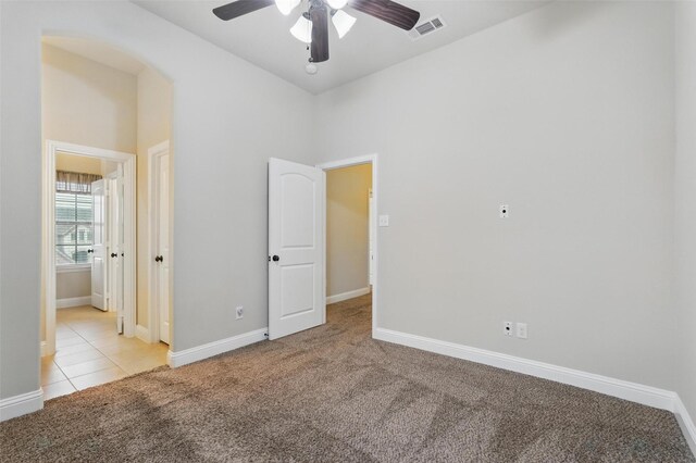 unfurnished bedroom featuring visible vents, light carpet, baseboards, a ceiling fan, and light tile patterned floors
