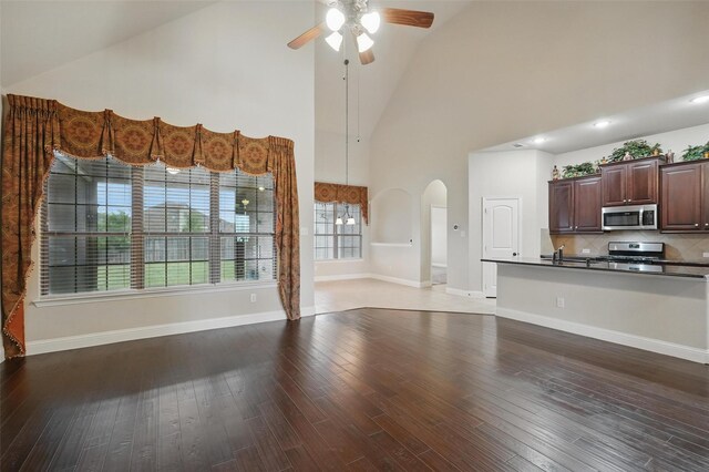 unfurnished living room with ceiling fan, arched walkways, high vaulted ceiling, baseboards, and wood finished floors