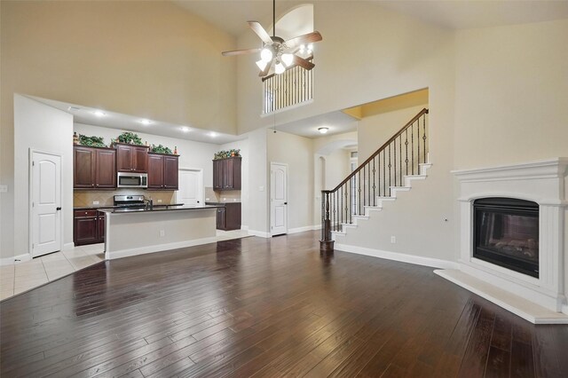 unfurnished living room with wood-type flooring, high vaulted ceiling, a glass covered fireplace, and ceiling fan