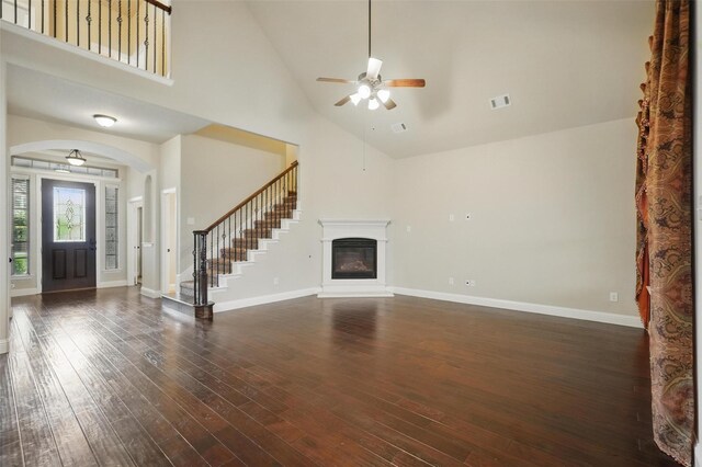 unfurnished living room with a ceiling fan, visible vents, stairway, high vaulted ceiling, and dark wood-style floors