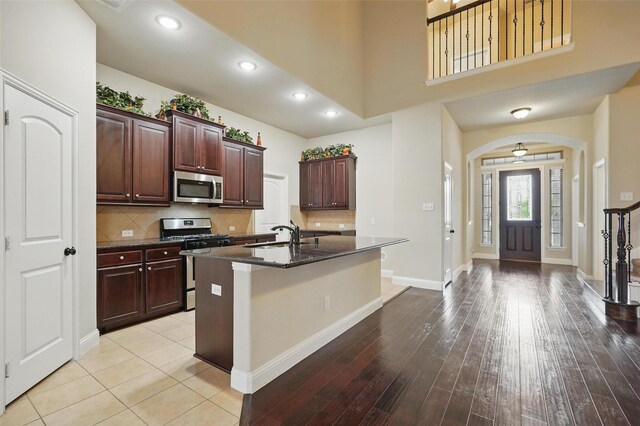 kitchen featuring decorative backsplash, arched walkways, a center island with sink, a sink, and stainless steel appliances