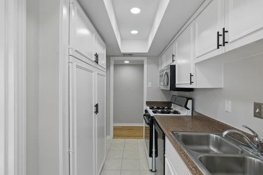 kitchen featuring a sink, white cabinetry, light tile patterned floors, range with gas cooktop, and dark countertops