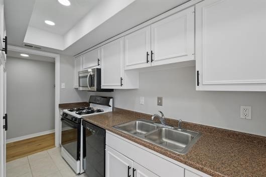 kitchen featuring black dishwasher, a sink, stainless steel microwave, white cabinetry, and range with gas cooktop