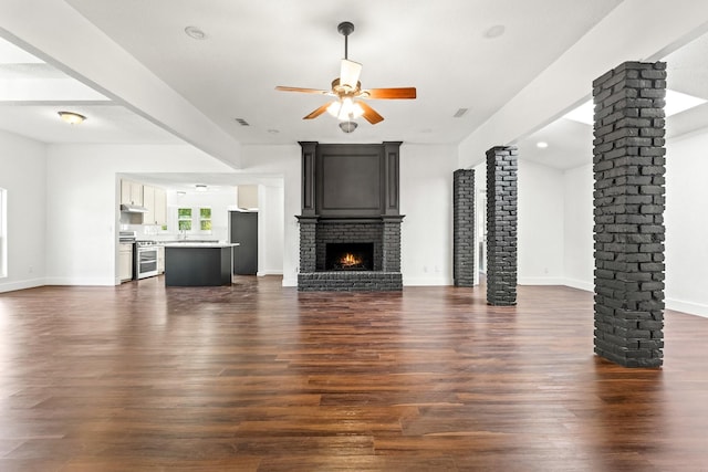 3005 Club Hill Dr, Garland, TX 75043 - unfurnished living room featuring baseboards, decorative columns, a fireplace, dark wood-style flooring, and ceiling fan