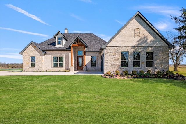 french country home featuring a front yard, stone siding, roof with shingles, and a chimney