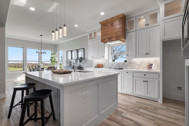 kitchen featuring light stone countertops, an island with sink, crown molding, a notable chandelier, and tasteful backsplash