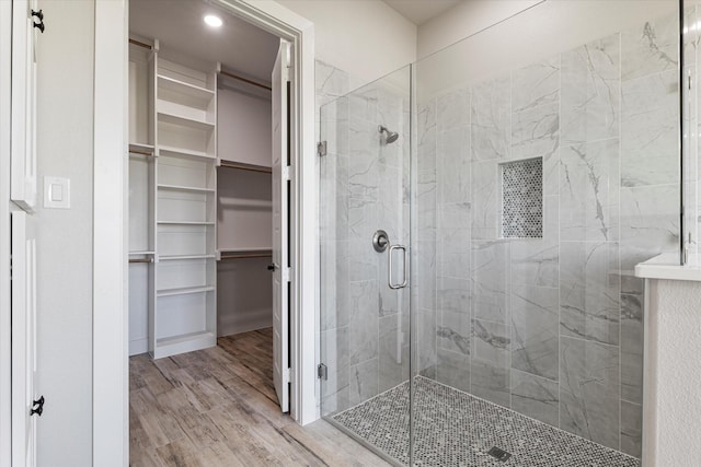 bathroom featuring a shower stall, a walk in closet, and wood finished floors