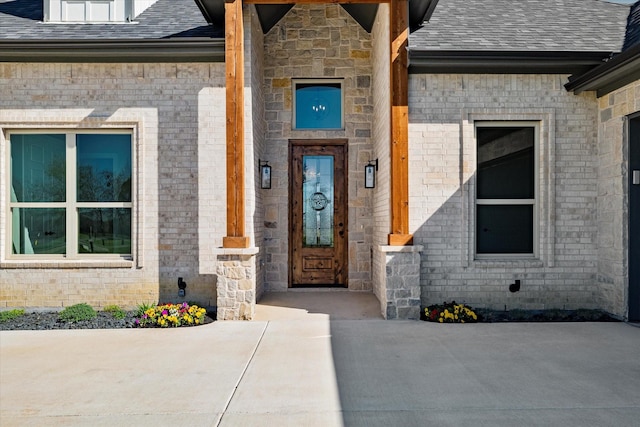 property entrance featuring brick siding and a shingled roof