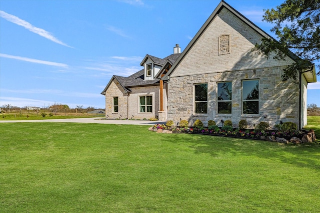 rear view of house with stone siding, a chimney, and a yard