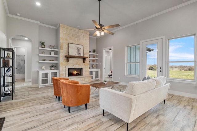 living room with crown molding, baseboards, arched walkways, and light wood finished floors