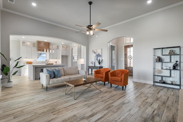 living area featuring arched walkways, a healthy amount of sunlight, light wood finished floors, and a ceiling fan