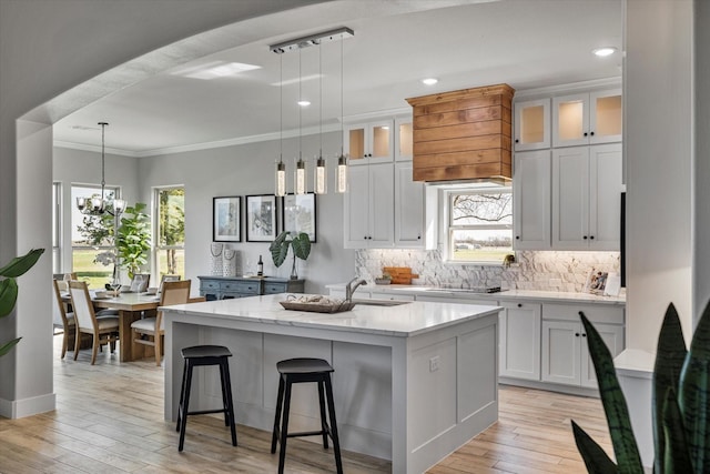 kitchen with light wood finished floors, backsplash, an island with sink, and ornamental molding