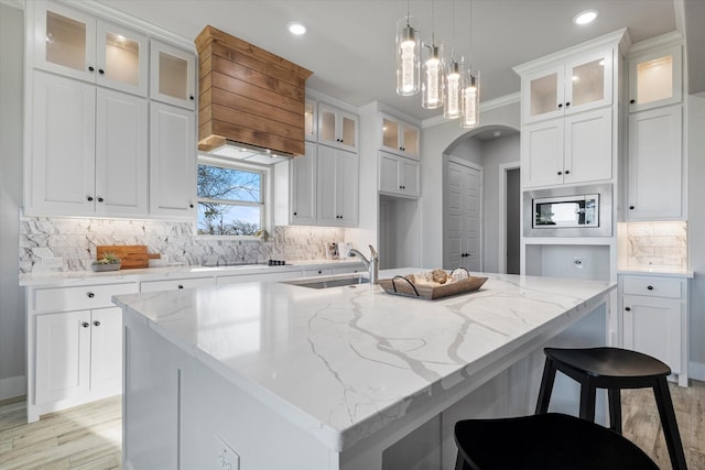 kitchen with arched walkways, a kitchen island with sink, a sink, crown molding, and stainless steel microwave