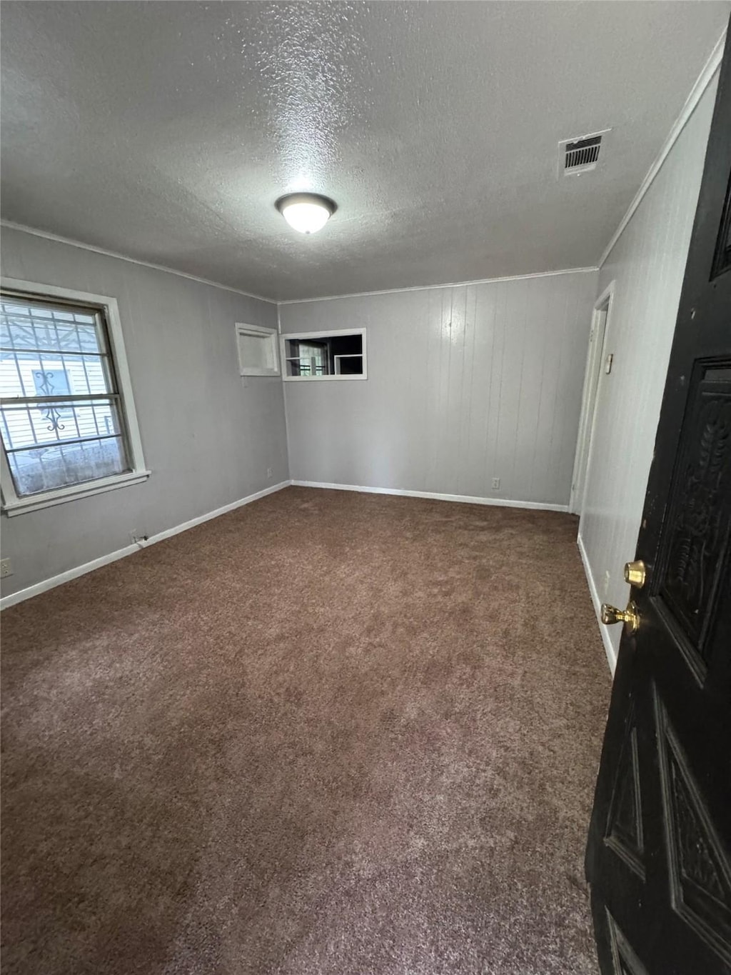 empty room featuring a textured ceiling, dark carpet, baseboards, and ornamental molding