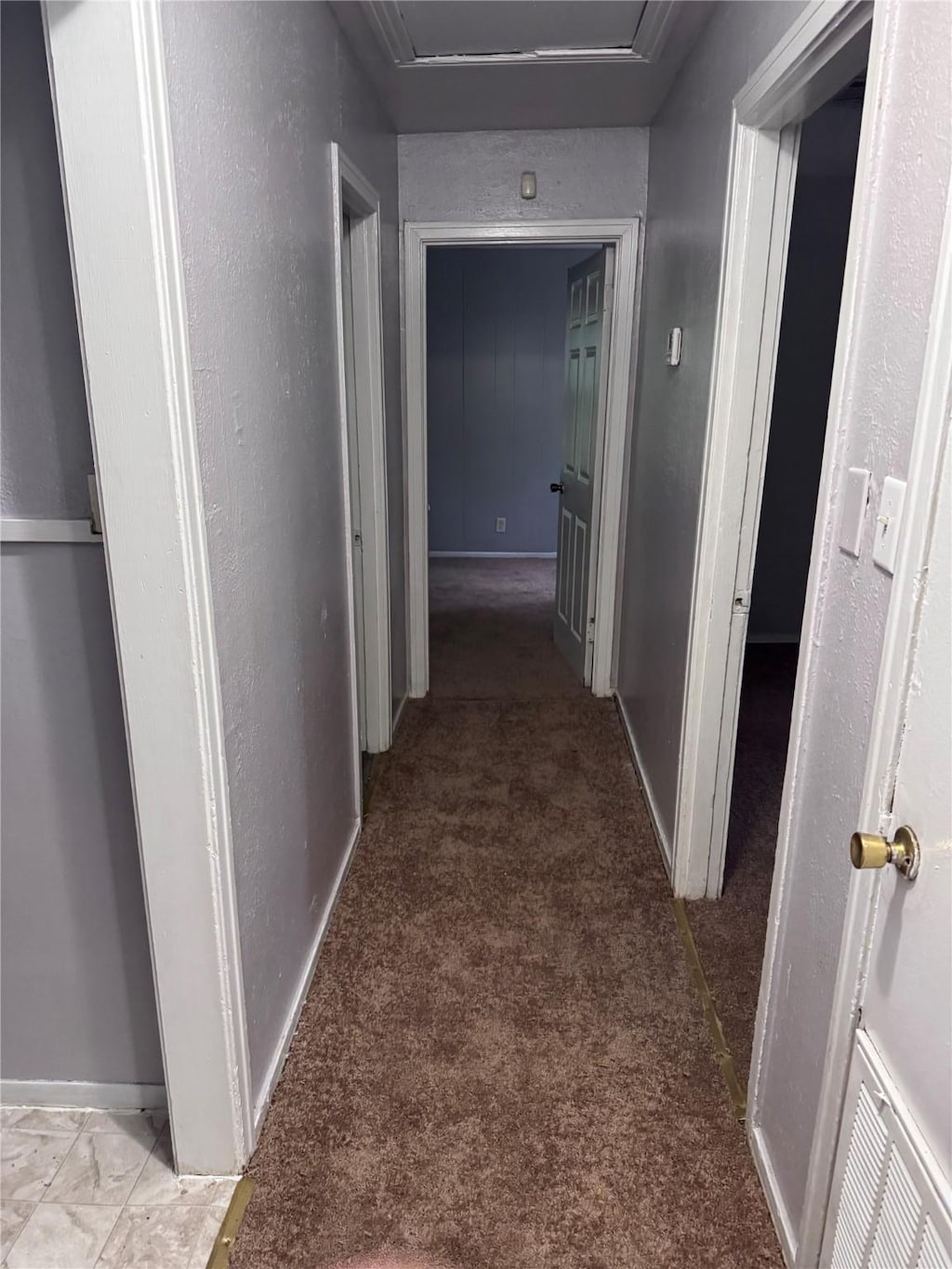 hallway with attic access, light colored carpet, and baseboards