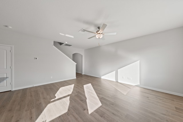unfurnished living room with baseboards, arched walkways, wood finished floors, and a ceiling fan