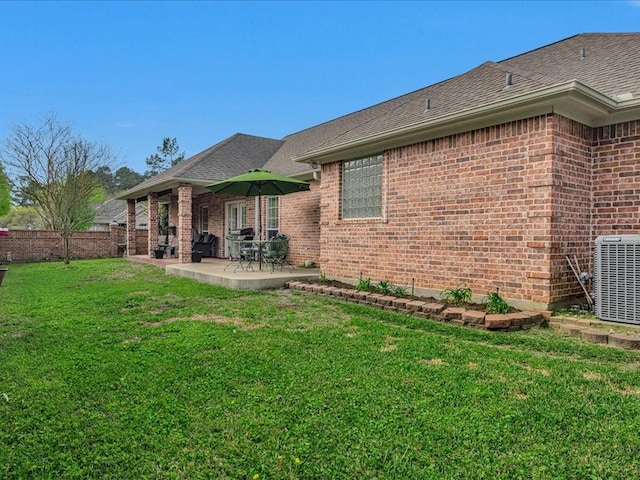 back of house with a patio area, a shingled roof, a lawn, central AC, and brick siding