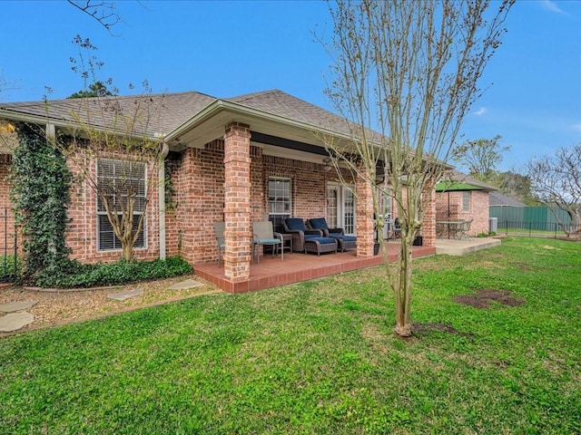 back of house with a yard, brick siding, fence, a patio area, and roof with shingles