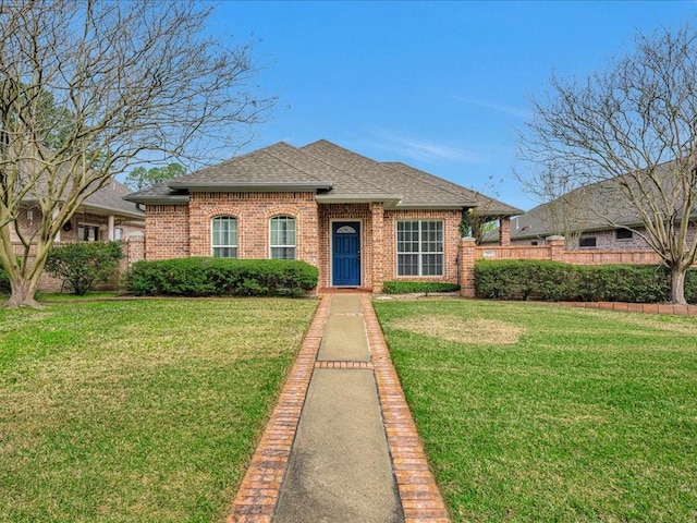 view of front of property featuring brick siding, fence, a front yard, and roof with shingles