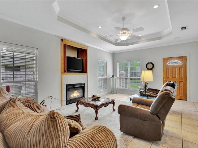 living room with light tile patterned floors, ceiling fan, a tray ceiling, visible vents, and ornamental molding