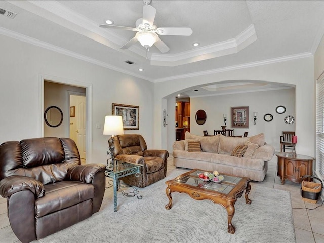 living area with arched walkways, ceiling fan, ornamental molding, and a raised ceiling