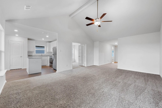 unfurnished living room featuring ceiling fan, beamed ceiling, high vaulted ceiling, and light carpet