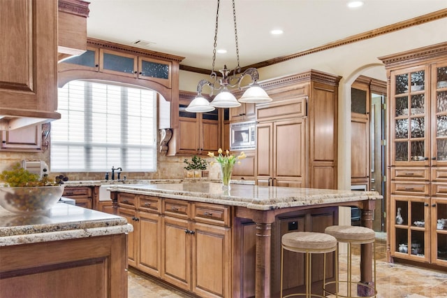 kitchen with stainless steel microwave, a kitchen island, crown molding, a breakfast bar area, and light stone counters