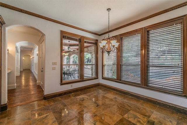 unfurnished dining area with stone finish flooring, baseboards, ornamental molding, arched walkways, and a notable chandelier