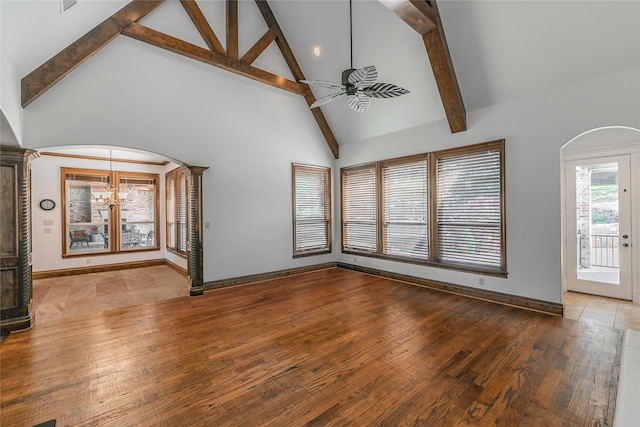 unfurnished living room featuring ceiling fan, beamed ceiling, arched walkways, high vaulted ceiling, and wood-type flooring