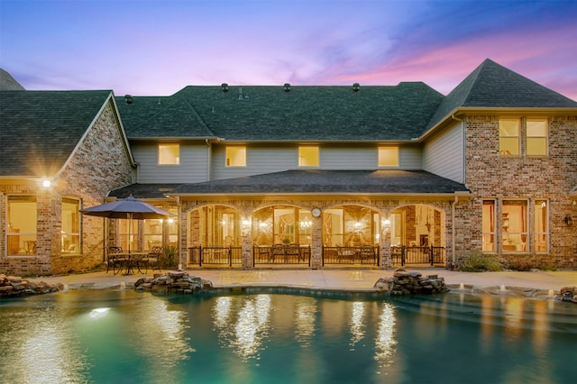 rear view of house with brick siding, an outdoor pool, a patio, and roof with shingles