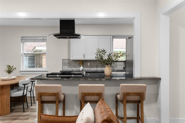 6410 Symphony Ln, Dallas, TX 75227 - kitchen with ventilation hood, light wood-style flooring, white cabinets, a kitchen breakfast bar, and plenty of natural light