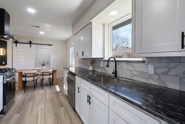kitchen with a sink, a barn door, dark stone countertops, light wood-style flooring, and gas range oven