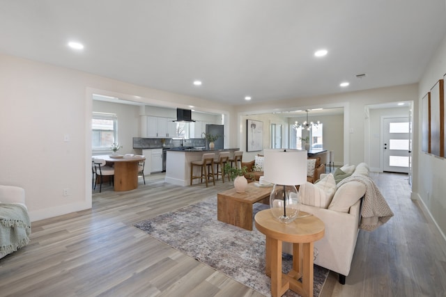 living area with an inviting chandelier, plenty of natural light, light wood finished floors, and baseboards
